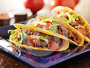 Three beef tacos with cheese, lettuce and tomatoes