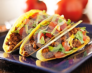 Three beef tacos with cheese, lettuce and tomatoes