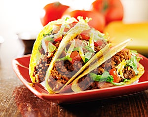 Three beef tacos with cheese, lettuce and tomatoes
