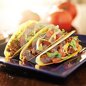 Three beef tacos with cheese, lettuce and tomatoes