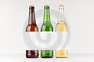 Three beer bottles longneck 500ml different colors with blank white label on white wooden board, mock up.