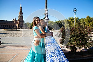 Three belly dancers dressed in light blue leaning on the railing of a bridge. They are talking to each other and looking at the