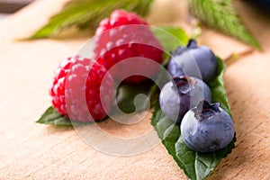 Three big blue blueberries on green leaf with red raspberries