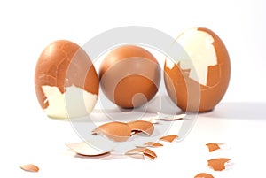 Three big brown eggs is cracking on white background having pieces of egg shell around them, food ingredient for cooking