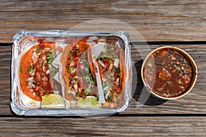 Three Birria Tacos with Limes in a Takeout Container with a Side of Consomme