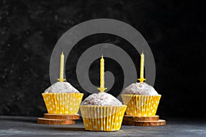 Three birthday cupcakes in paper cups with extinguished birthday candles on dark background