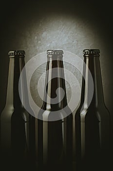 three black bottles of beer on a dark background with light/three black bottles of beer on a dark background with light. Selective