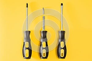 three black and yellow screwdrivers on a yellow background with space for text. Tools, construction and workshop, home
