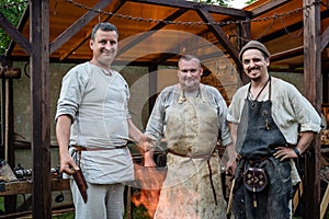 Three blacksmiths posing in front of a workshop in the open air.