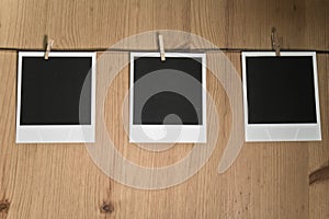 Three blank instant photos hanging on clothesline on wooden background, art concept