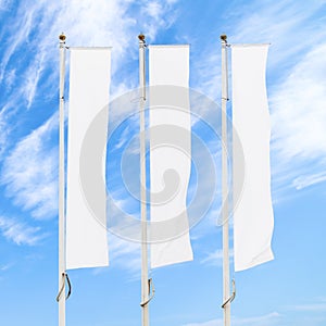 Three blank white corporate flags on flagpoles against cloudy blue sky