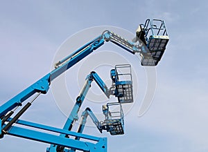 Three blue aerial work platform of cherry pickers, against blue cloudy sky