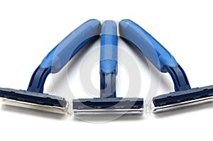 Three blue and green plastic one use disposable shavers white backdrop