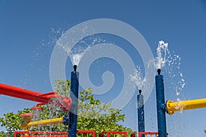 Three blue spray water park sprinklers spraying water above for children`s summer fun