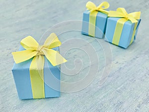 Three blue square gift boxes, one is isolated in front of the two, on blue green watercolor textured background.