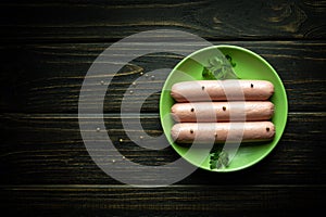 Three boiled sausages in a green plate on a black table with spices and parsley for a delicious breakfast. Space for recipe or