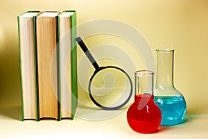 Three books, a magnifying glass and chemical flasks on a yellow background. Scientific research, study.