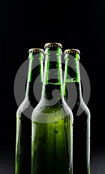Three bottles of beer from green glass on black background.