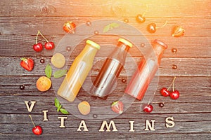 Three bottles of juice, fruit and inscription Vitamins. Wooden b