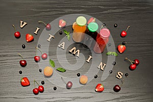 Three bottles with juice, fruits and inscription vitamins on a black wooden background, food concept