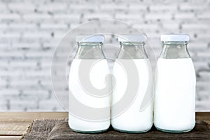 Three bottles of milk on a wooden table and white concrete wall background