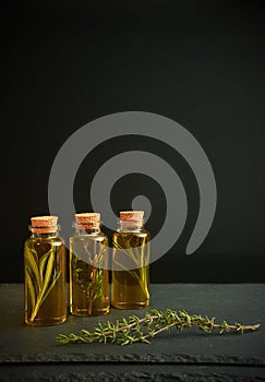 Three bottles of olive oil with herbs, thyme and rosemary and small twig on on a dark background. Space for text