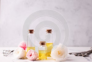 Three bottles with rose essential aroma oil and rose flowers on light  grey textured background.