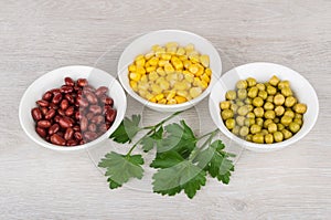 Three bowls with green peas, beans, sweet corn and parsley