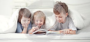 Three boy read book indoors on bed