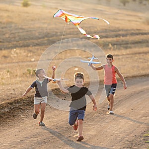Three boys of different ages, running on a dirt road, flying a kite and planes, summer outdoor games