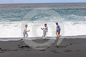 Three boys have fun at the black volcanic beach