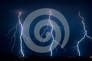 Three branched lightning bolts next to each other strike down to earth from a severe summer thunderstorm in The Netherlands