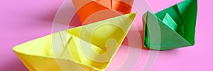 Three bright colorful multicolor paper origami boats in orange, yellow and green colors on a pink background. banner.