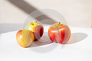 Three bright ripe red apples iin the light of the sun with long shadows on a white background. One apple of an unusual shape of an photo