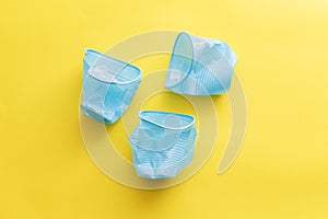 Three broken blue plastic disposable cups over a yellow background