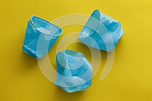 Three broken blue disposable plastic cups over a yellow background