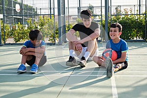 Three brothers laughing and sitting on the football court floor resting and talking after a match