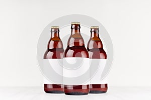 Three brown belgian steinie beer bottles 500ml with blank white label on white wooden board, mock up.