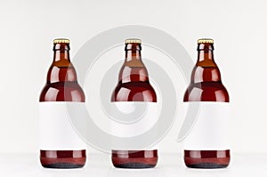 Three brown belgian steinie beer bottles 500ml with blank white label on white wooden board, mock up.