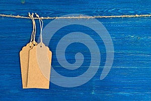 Three brown blank paper price tags or labels set hanging on a rope on the blue background.