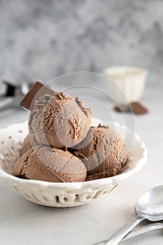 Three brown chocolate ice cream balls, scoops in white bowl on gray background