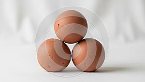 Three brown eggs are arranged in a triangular formation on a smooth white