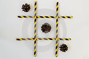 Three brown fir cones lie in a row in a tic-tac-toe game, in a grid on a white background. The grid consists of colored tubes from