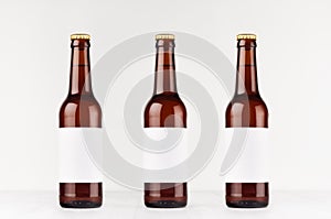 Three brown longneck beer bottles 330ml with blank white label on white wooden board, mock up.