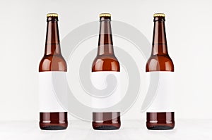 Three brown longneck beer bottles 500ml with blank white label on white wooden board, mock up.