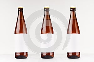 Three brown NRW beer bottles 500ml with blank white label on white wooden board, mock up.