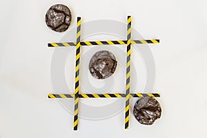 Three brown pastry cakes are in a row in a tic-tac-toe game, in a grid on a white background. The grid consists of colored tubes