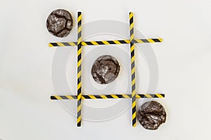 Three brown pastry cakes are in a row in a tic-tac-toe game, in a grid on a white background. The grid consists of colored tubes