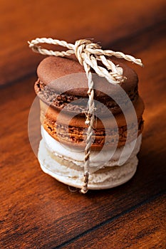 Three brown and white french macarons or macaroons tighten together with a natural string over a vintage wood background.