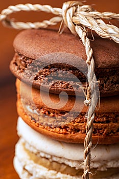 Three brown and white french macarons or macaroons, tighten together with a natural string over a wooden background